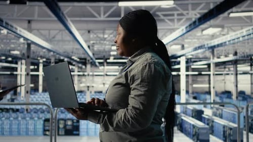 IT Expert Monitors Server Farm Activity Using Laptop While Walking in Facility