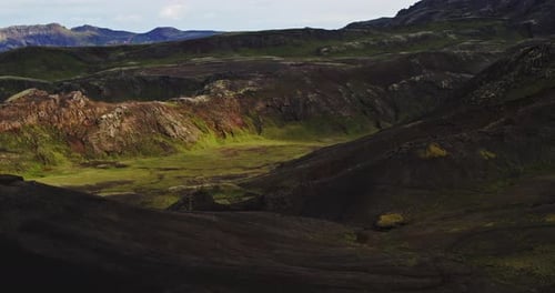 Pull back drone shot of a mountain valley in Iceland, as bright green moss and volcanic black sand c