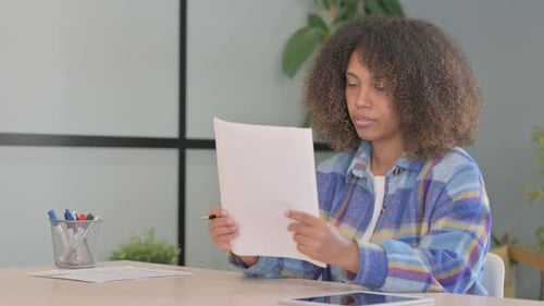 Woman Reads Paperwork, Smiles at Her Desk