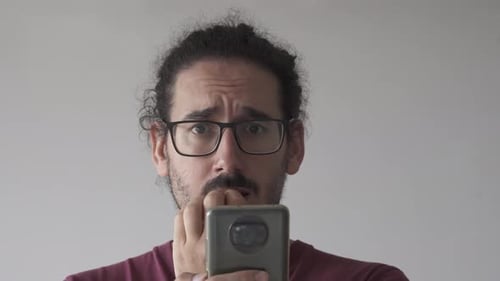 Close up of anxious man with smartphone biting his nails and looking at camera