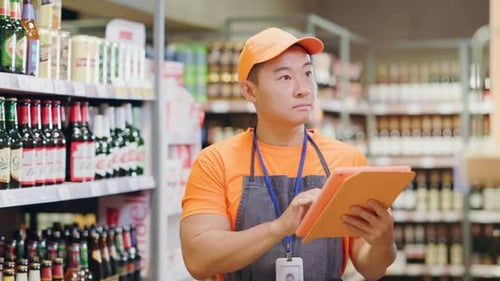 Concentrated Asian Worker in Apron Using Digital Tablet Counting Bottles Controlling Number Quality