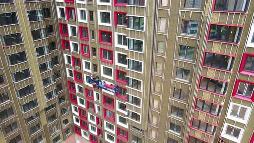 Arbeiter in einer Wiege montieren die Fensterverkleidung eines im Bau befindlichen Gebäudes