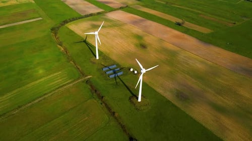 Drone shot of two working wind turbines and a few solar panels producing green electric energy on a