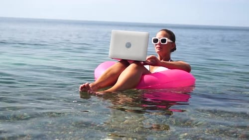 Woman Freelancer Works on Laptop Swimming in Sea on Pink Inflatable Ring Happy Tourist in Sunglasses