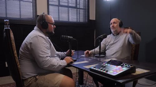 Men speak into microphones, recording audio podcast in digital studio