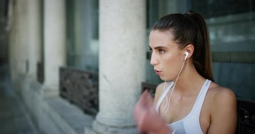 An attractive young woman taking a break while out for a jog in the city