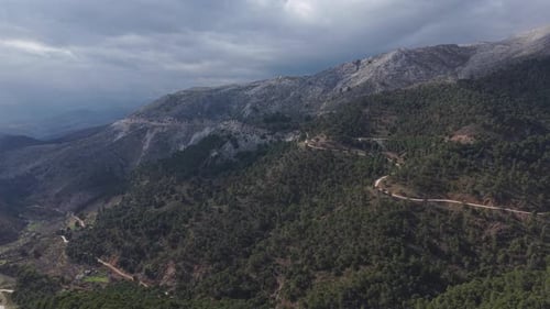 A scenic mountain landscape featuring forest-covered hills and a winding road cutting through the