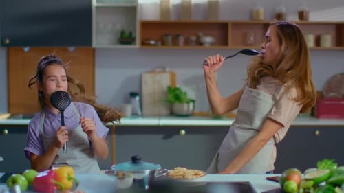 Mother and daughter sing in kitchen with spoons