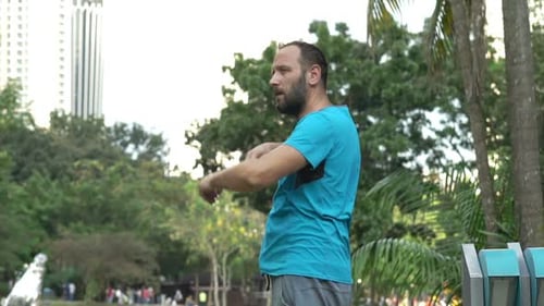 Young man stretching arms in the city park prepares for a morning workout
