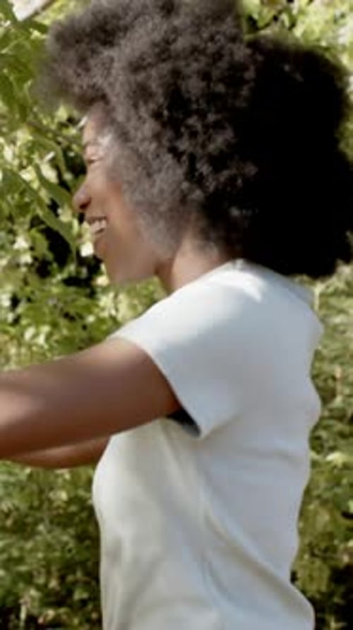Vídeo vertical: Mulher sorridente estendendo a mão como parceira em uma camisa de coral que se estende debaixo da árvore