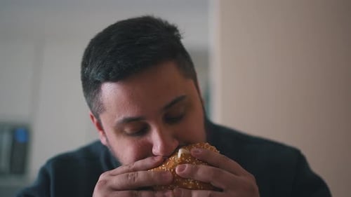 Adult Eating Burger in a Kitchen