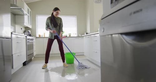 Happy caucasian woman cleaning floor with mop and bucket of water at home