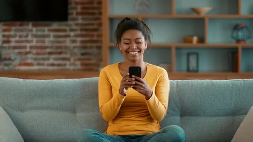 Smiling Woman Using Mobile Phone on Couch at Home