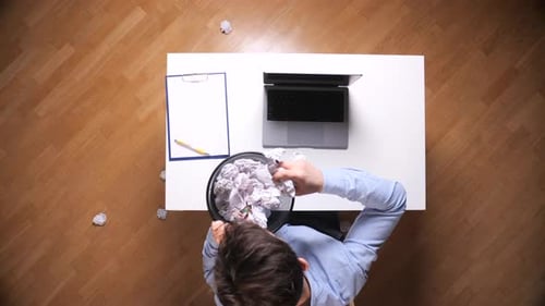 Man throwing crumpled paper into overflowing waste basket