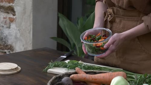 Woman in brown clothes cooking vegetable salad, holds glass plate win hands, Wroclaw, Poland