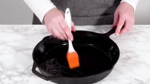 Graisser une poêle en fonte avec de l'huile d'olive pour préparer une frittata aux épinards et au jambon