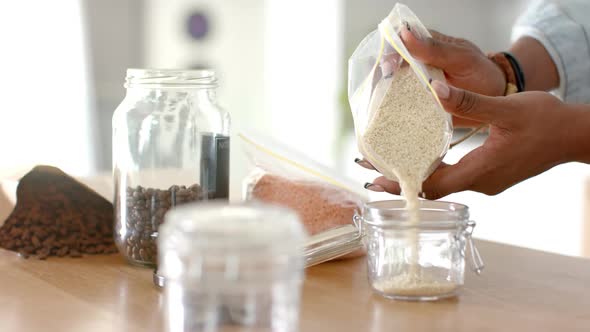 Pouring rice into glass jar, woman organizing pantry with various ...