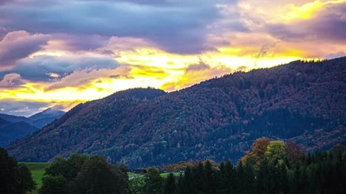 Timelapse of clouds rolling over wooded mountains and valley at sunset.