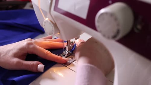Woman sewing blue fabric with professional machine in workshop, closeup
