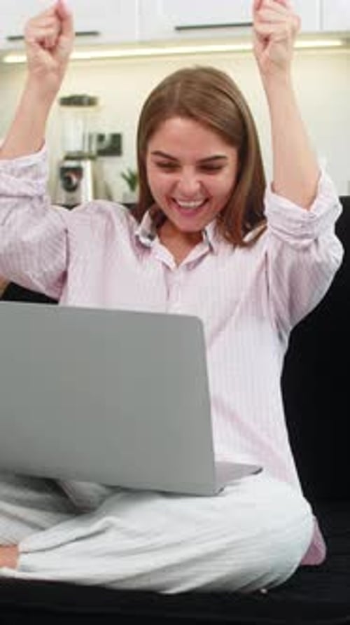 Excited Young Woman Cheering While Using Laptop Indoors