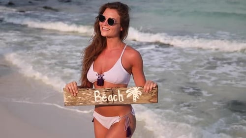 Frau trägt Badeanzug mit altem Holzschild am Strand