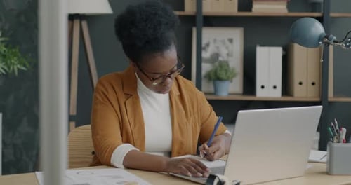 Portrait of Business Owner Wearing Glasses Using Laptop Typing and Writing Financial Imformation in