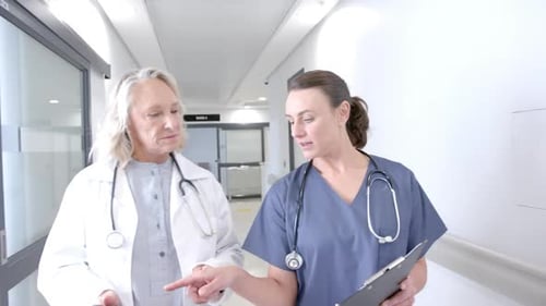 Caucasian female doctors in discussion using tablet in hospital corridor, slow motion