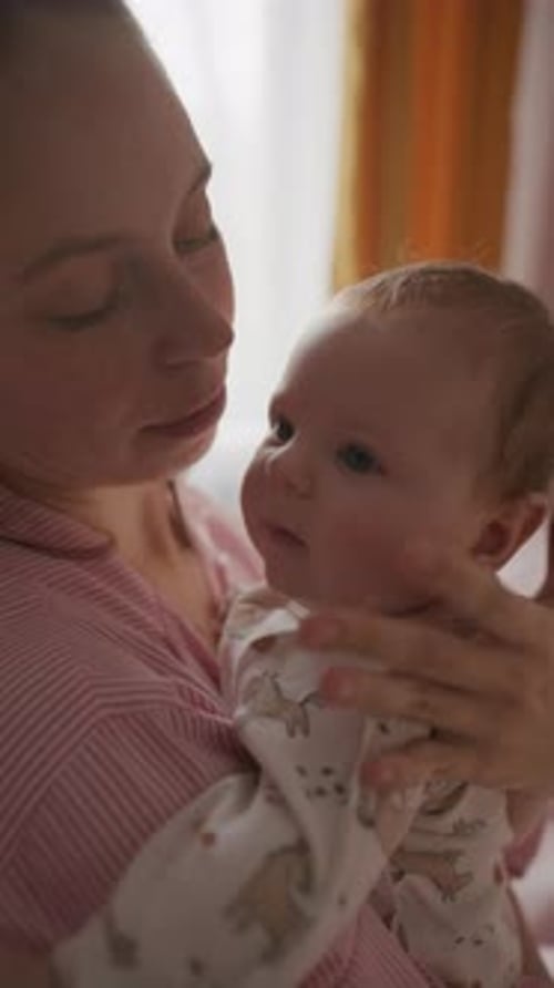 Young Mother Holding and Kissing Baby on Forehead at Home