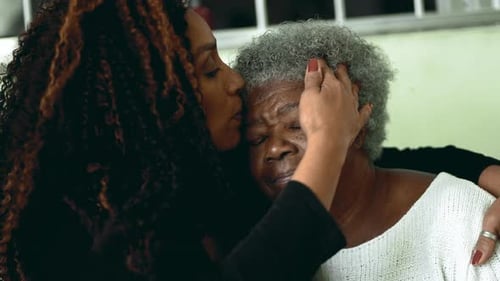 Affectionate Woman Hugging and Kissing Senior Woman Indoors