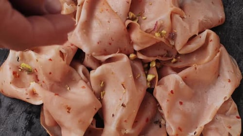 Adding pistachios to sliced mortadella Italian meat