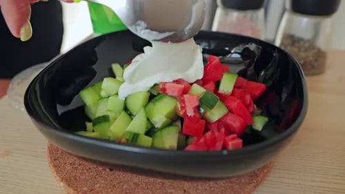 Slow Motion Sour Cream Added to Fresh Tomato Cucumber Salad, Black Bowl Close Up