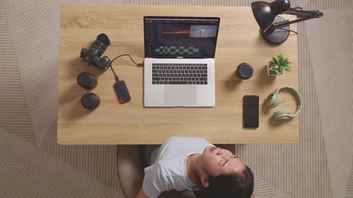 Vista superior de una editora asiática con auriculares que tiene dolor de espalda mientras usa una computadora portátil editando