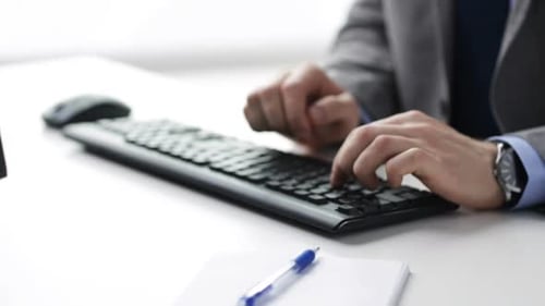 Businessman hands typing on computer keyboard and writing notes at office workplace
