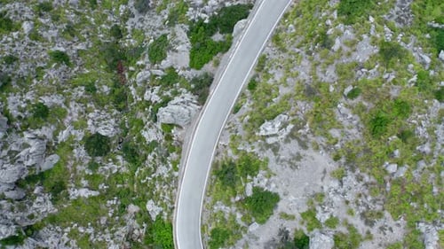 Curvy lone road through green stony mountain range remote pass, drone aerial view