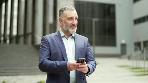 Successful senior investor with mobile phone outside office building Middle-aged businessman