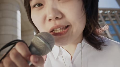 Asian Girl Singing in Microphone at Camera on City Street
