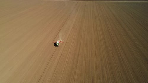Aerial view of a green Claas tractor seeding, sowing agricultural crops at field