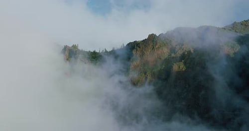 Incredibly beautiful scene, the top of a rocky mountain is covered with massive clouds and hides beh