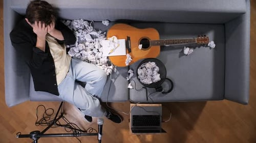 Young Musician Experiencing Writer's Block and Creative Frustration Covering Face While Lying on a