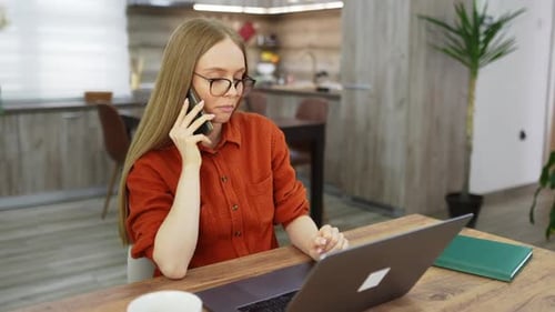 Woman Uses Laptop While Talking on Phone Indoors