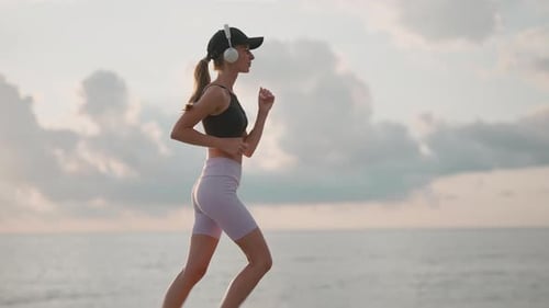 A Young Woman Runner is Listening to Music in Earphones and Training on a Sea Beach Close Up of