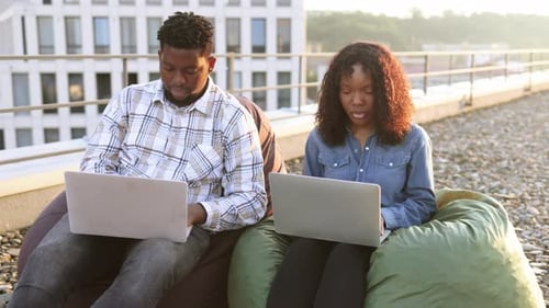 Man and Woman Working on Laptops on Rooftop
