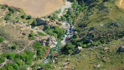 Aerial over the green mountains and a small water stream making its way between them, on a bright su