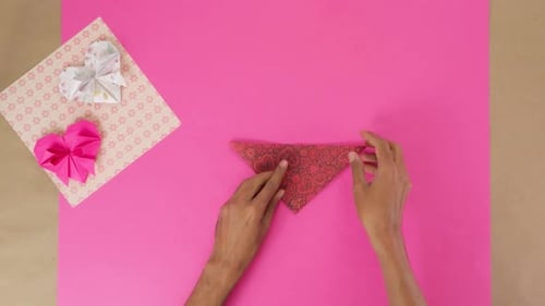 Folding a Paper Origami Heart on Pink Table