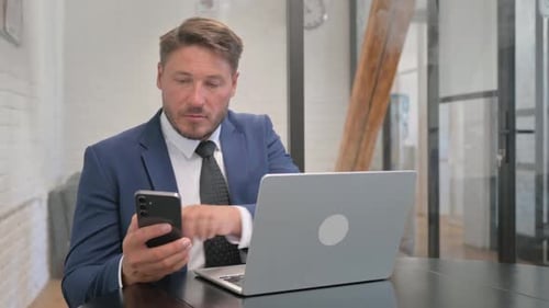 Man Working on Laptop and Using Smartphone