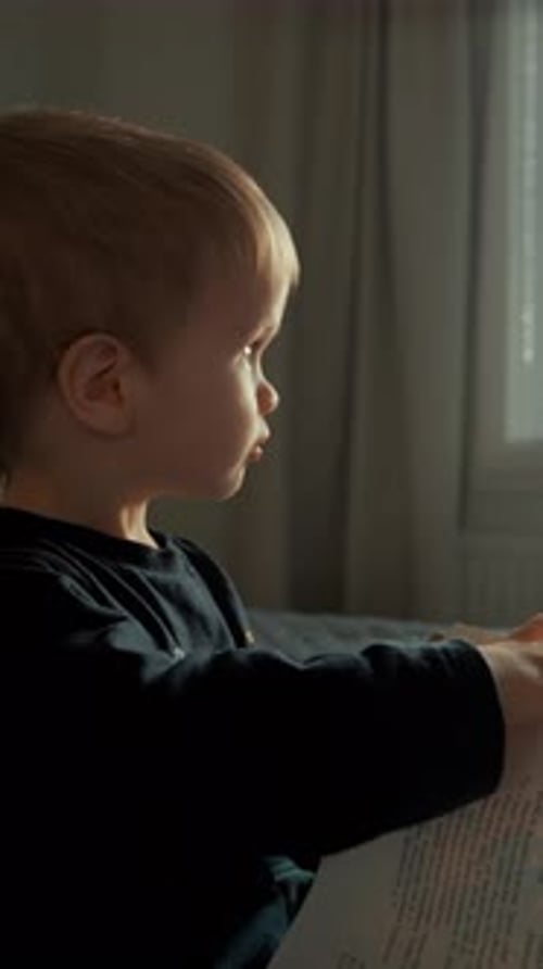 Vertical d'un petit garçon retourne les pages d'un livre en regardant par la fenêtre lumineuse