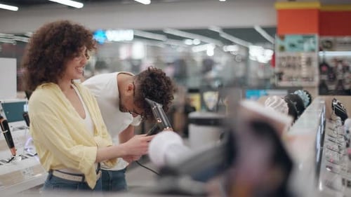 Happy couple choosing hair dryer in electronics store, slow motion