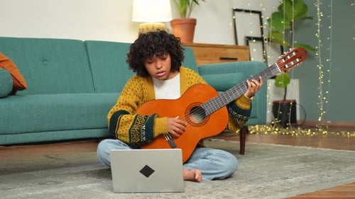 Young Woman Plays Guitar with Laptop at Home