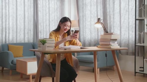 Young Woman Using Mobile Phone at Desk at Home