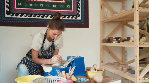Une potière vêtue d'un jean et d'un tablier travaille sur un tour de potier et fabrique un pot en céramique en argile